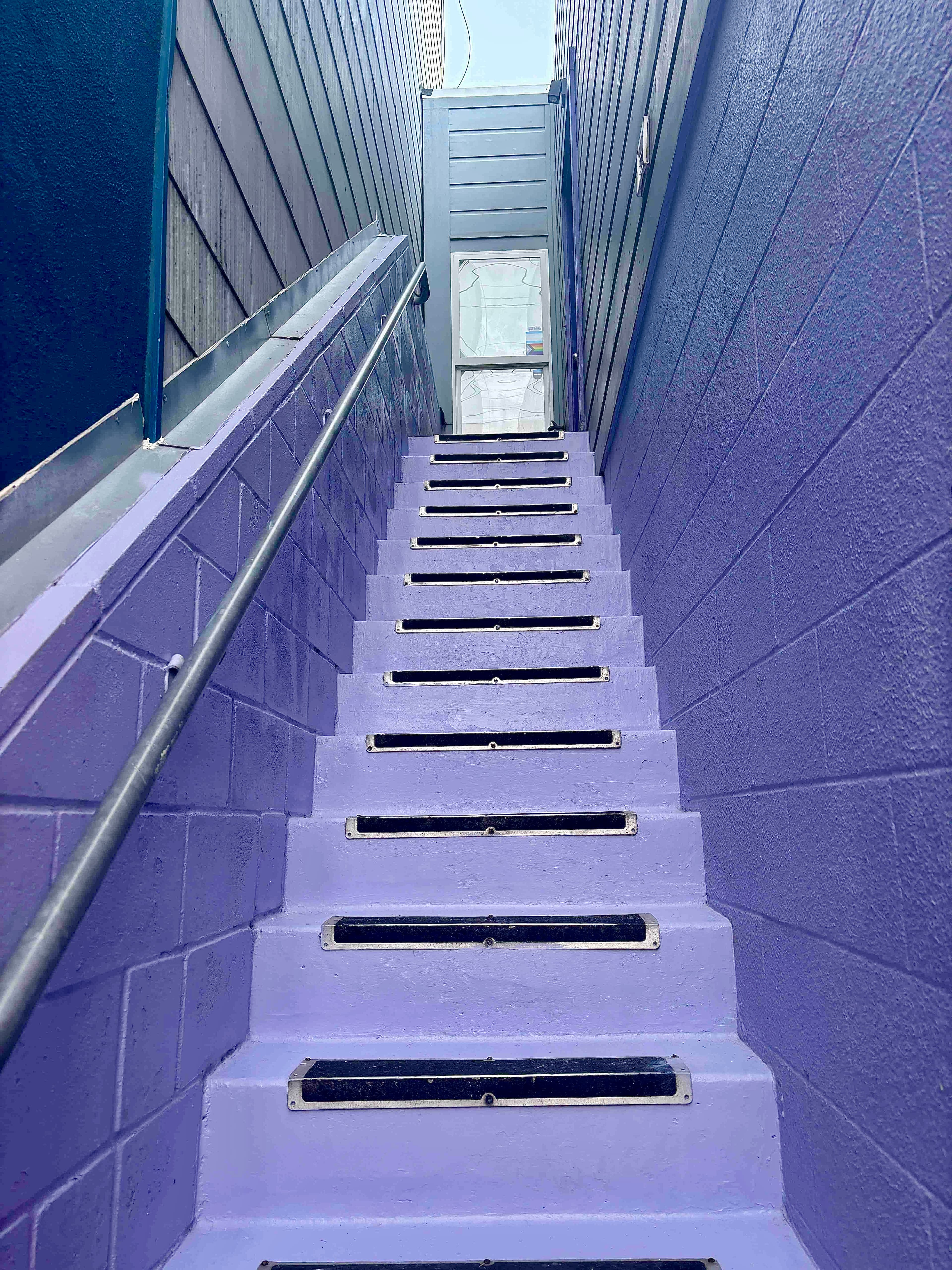 Narrow purple concrete stairs with black treads leading up to a white door.
