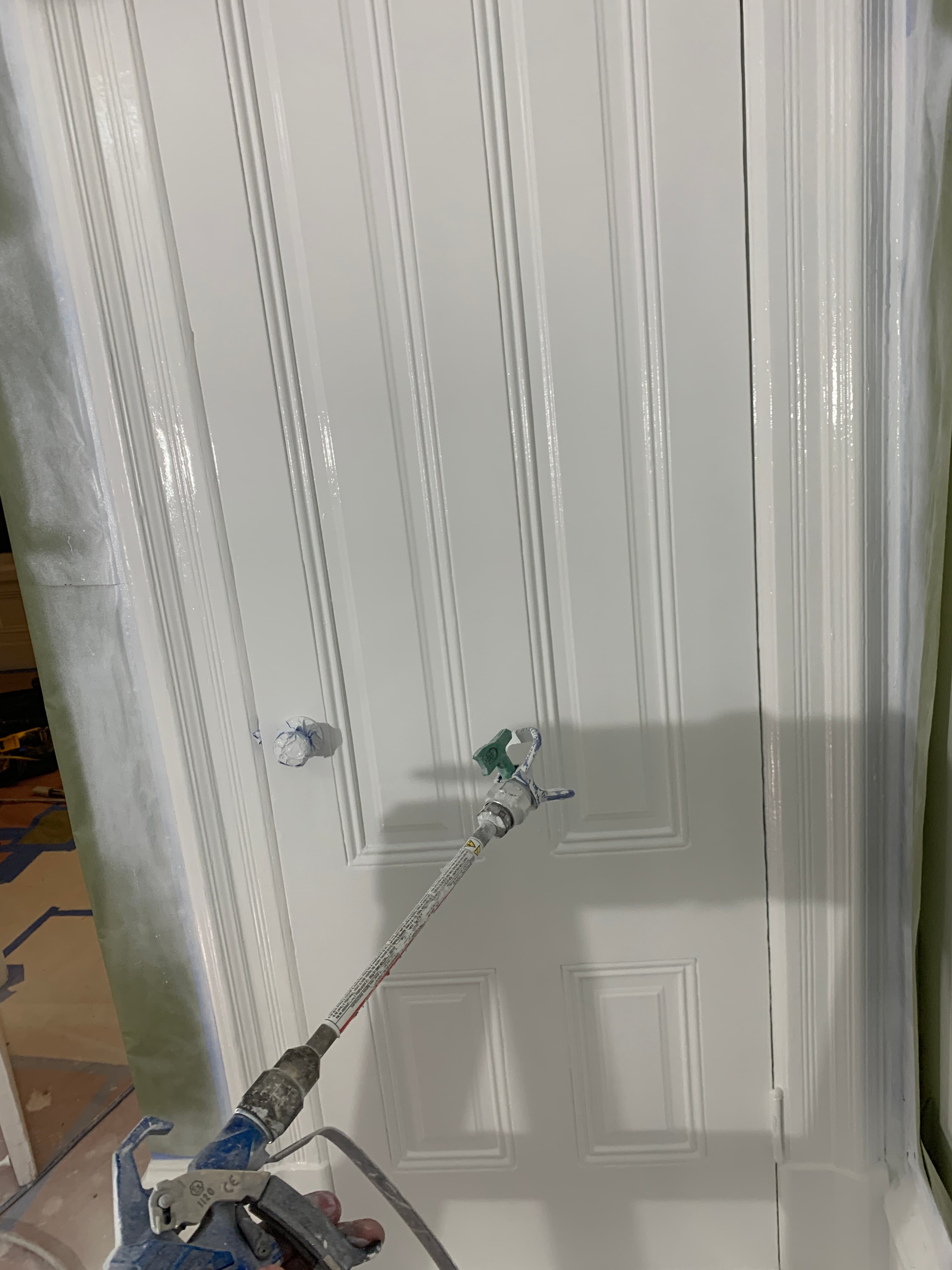 A professional spray gun applying a fresh coat of white paint to a paneled door.