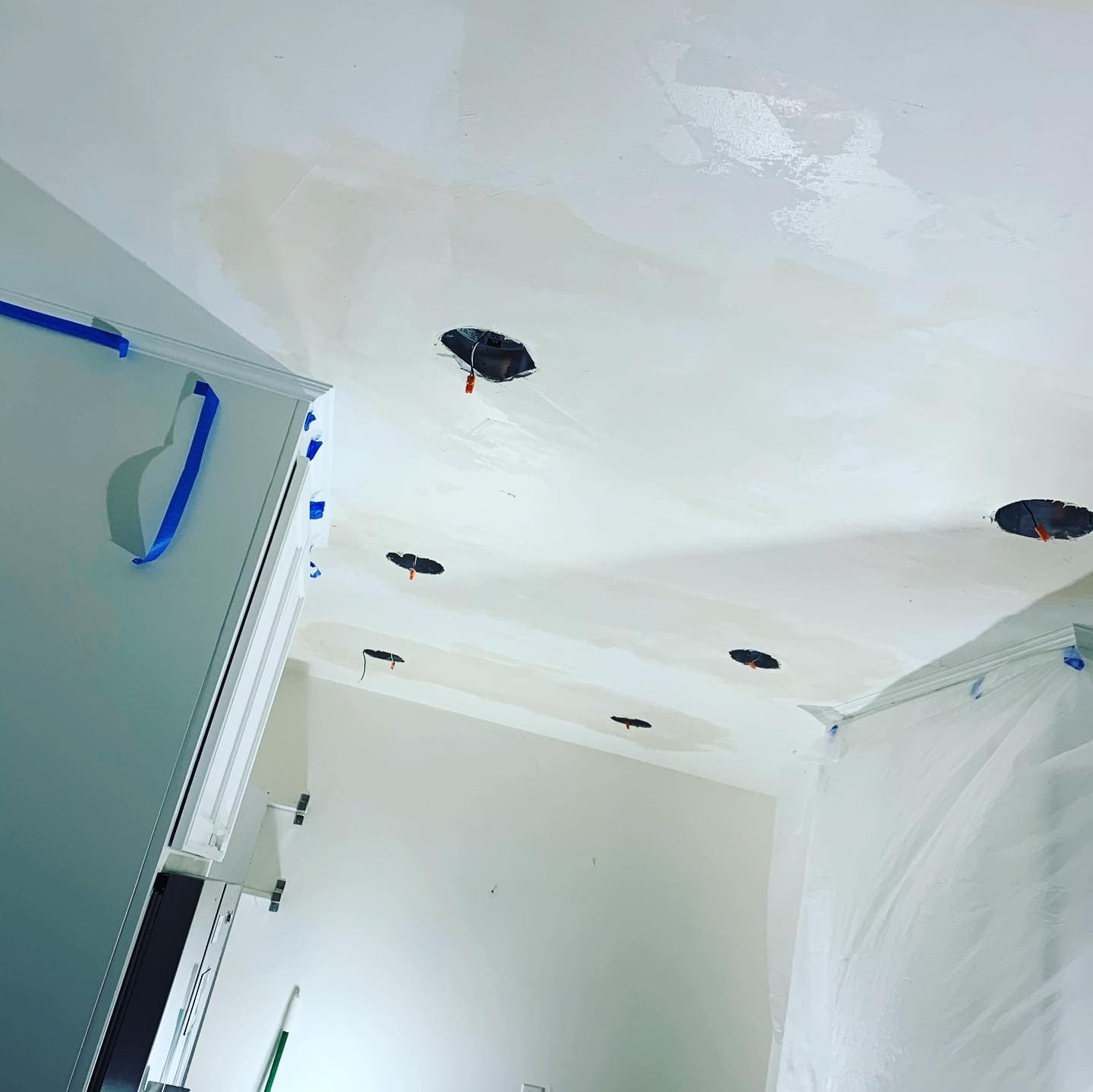 White ceiling under renovation with circular cutouts for recessed lighting and fresh plaster patches.