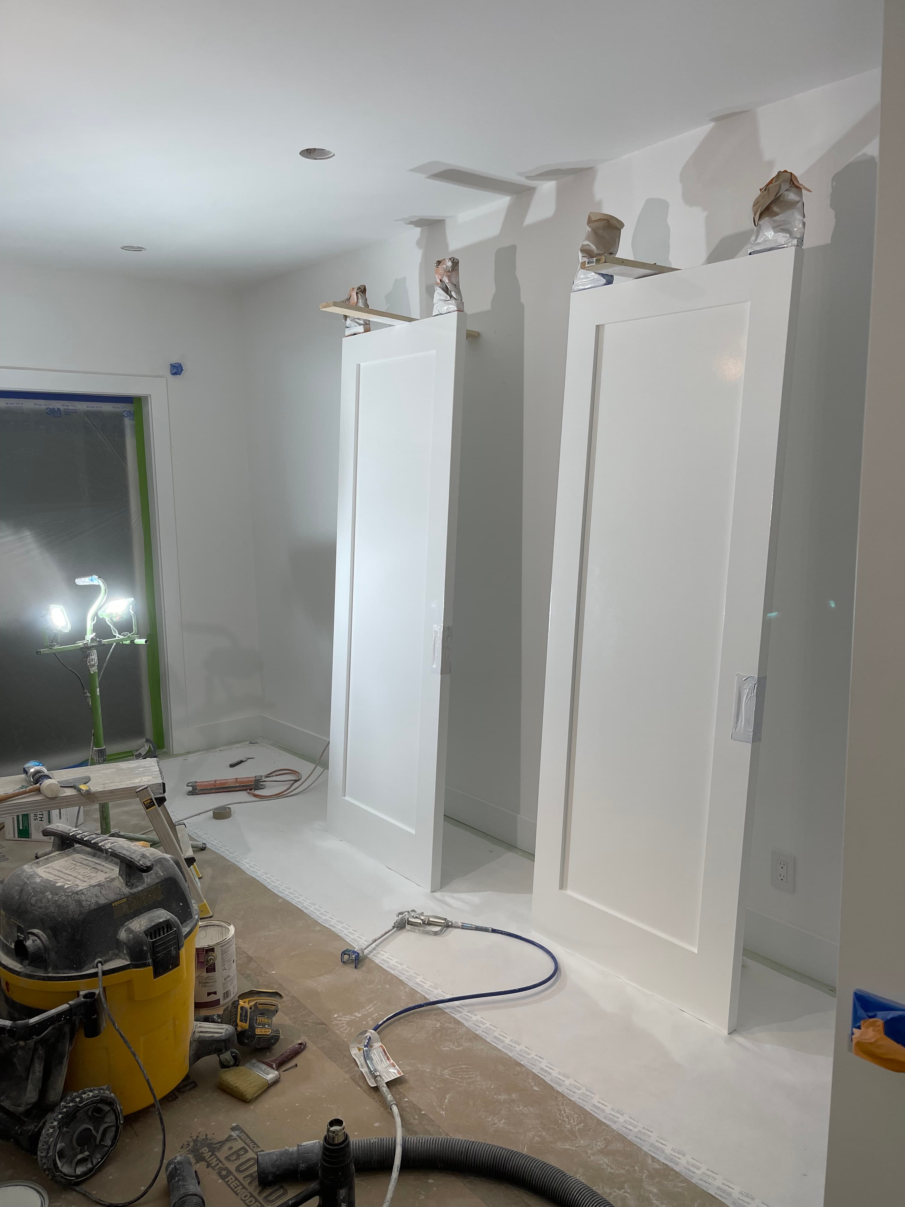 Freshly painted white shaker doors standing in a room under renovation with painting equipment.
