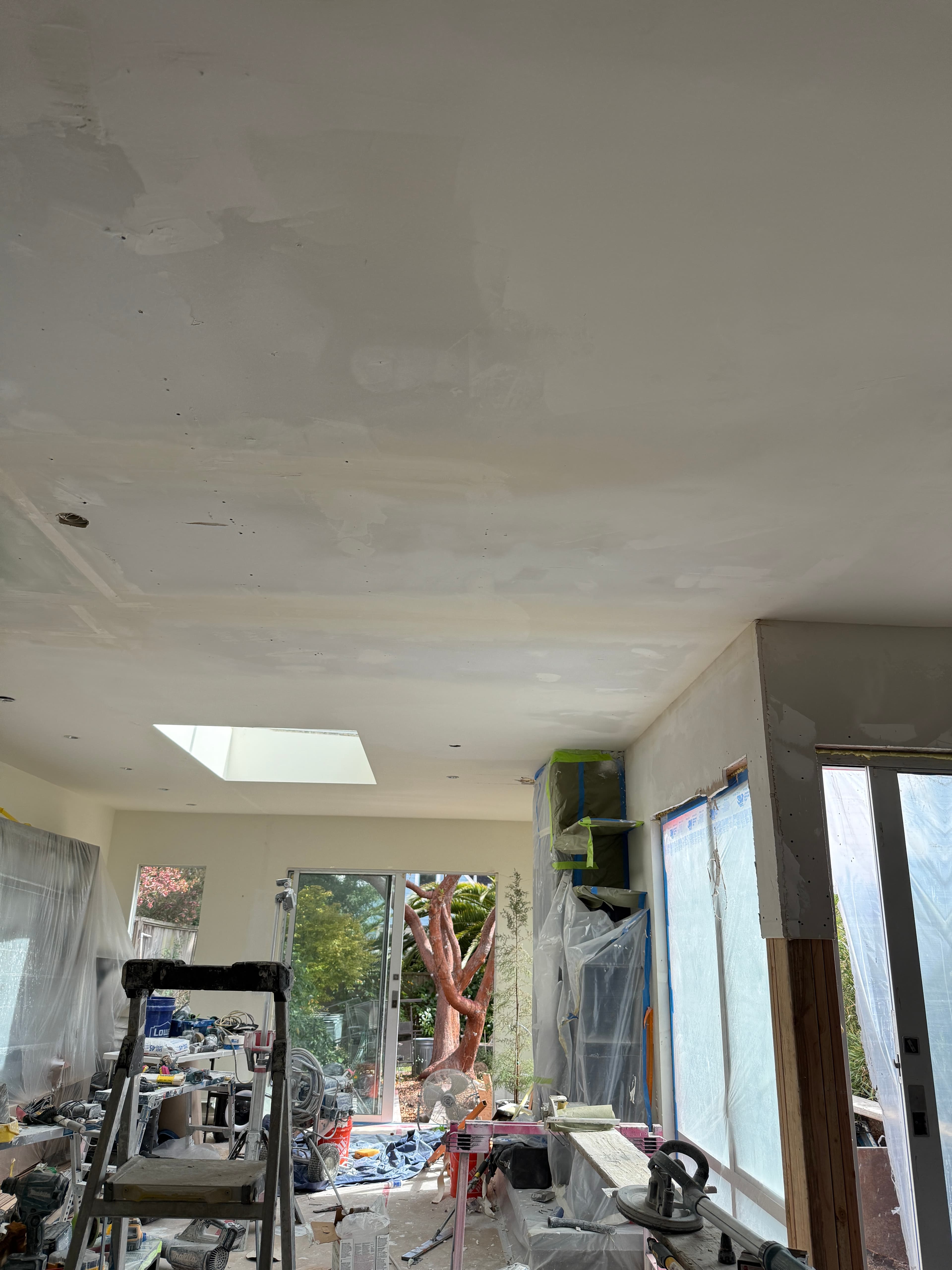 Room under renovation with a patched ceiling, skylight, and construction tools near sliding glass doors.
