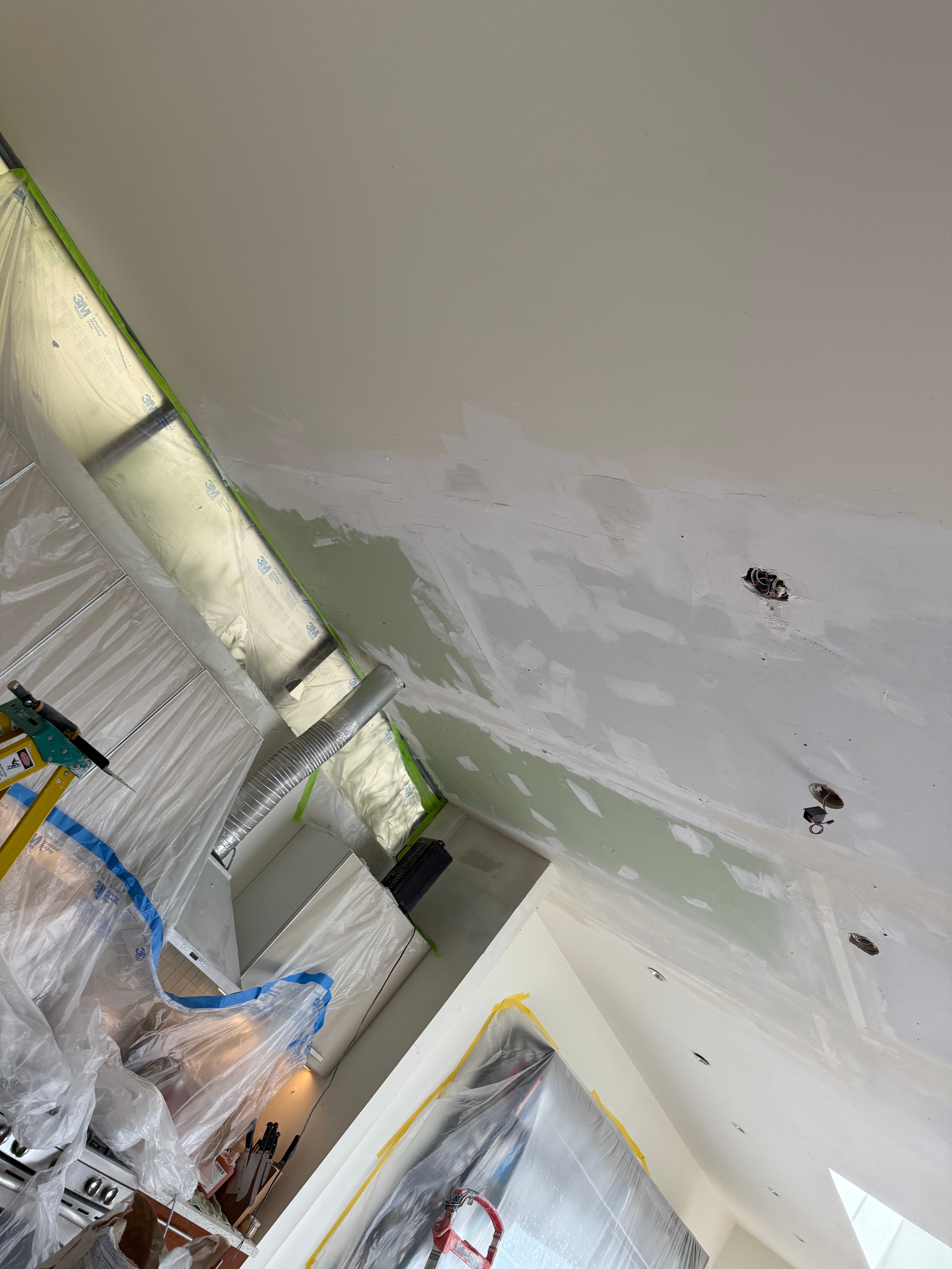 Drywall mud patches on a high ceiling above a kitchen protected by plastic sheeting.
