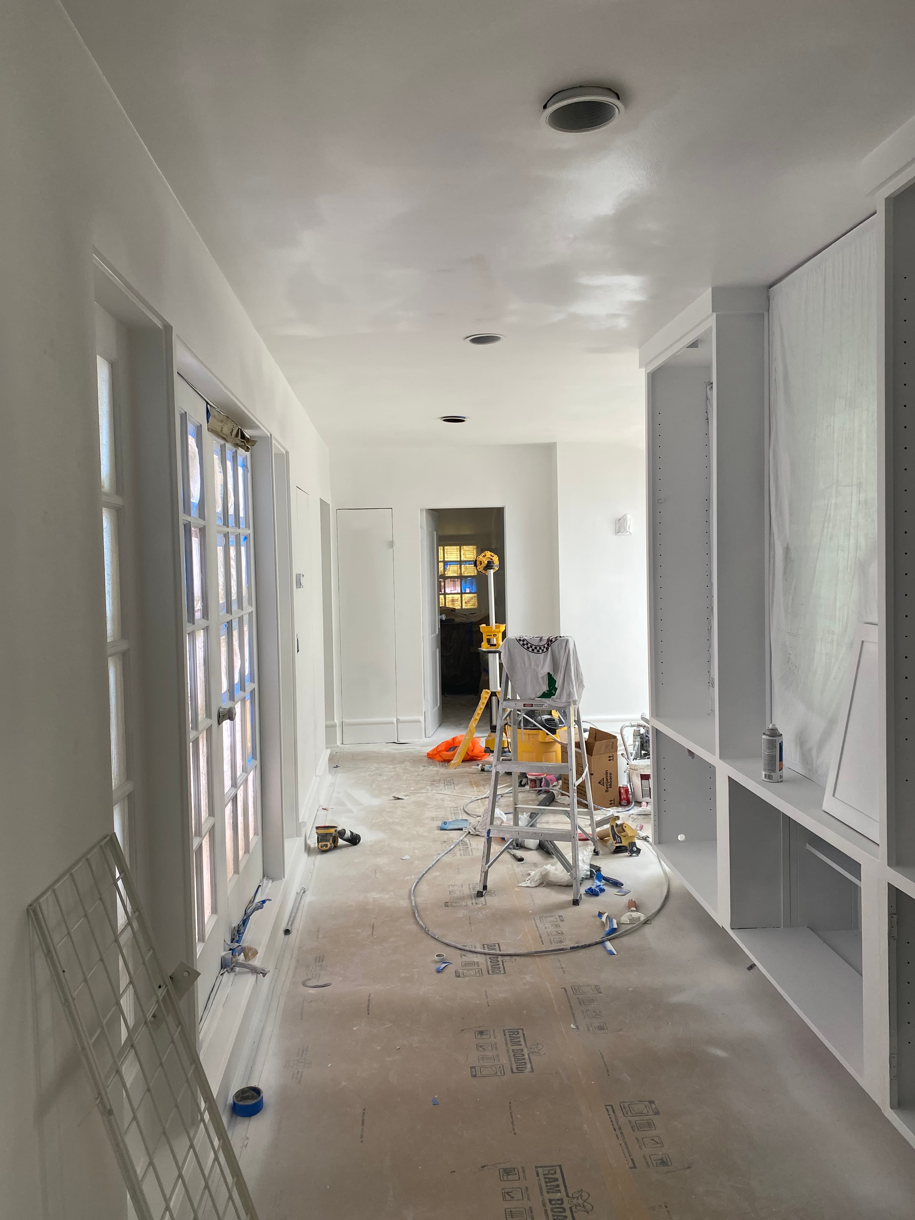 White interior under renovation featuring a ladder, construction tools, and protective floor covering.