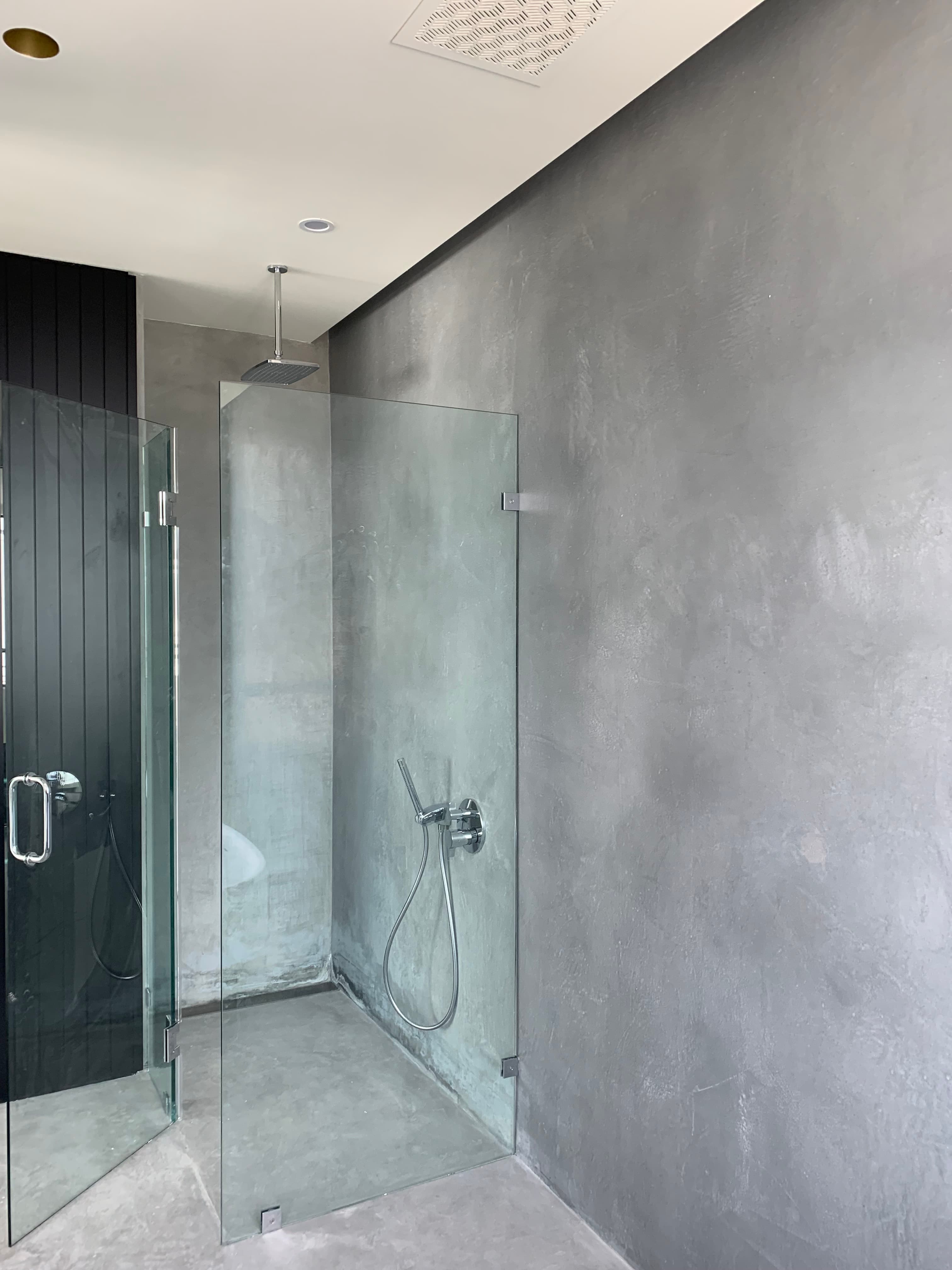 Top-down view of a modern shower with grey concrete walls, glass partition, and chrome fixtures.