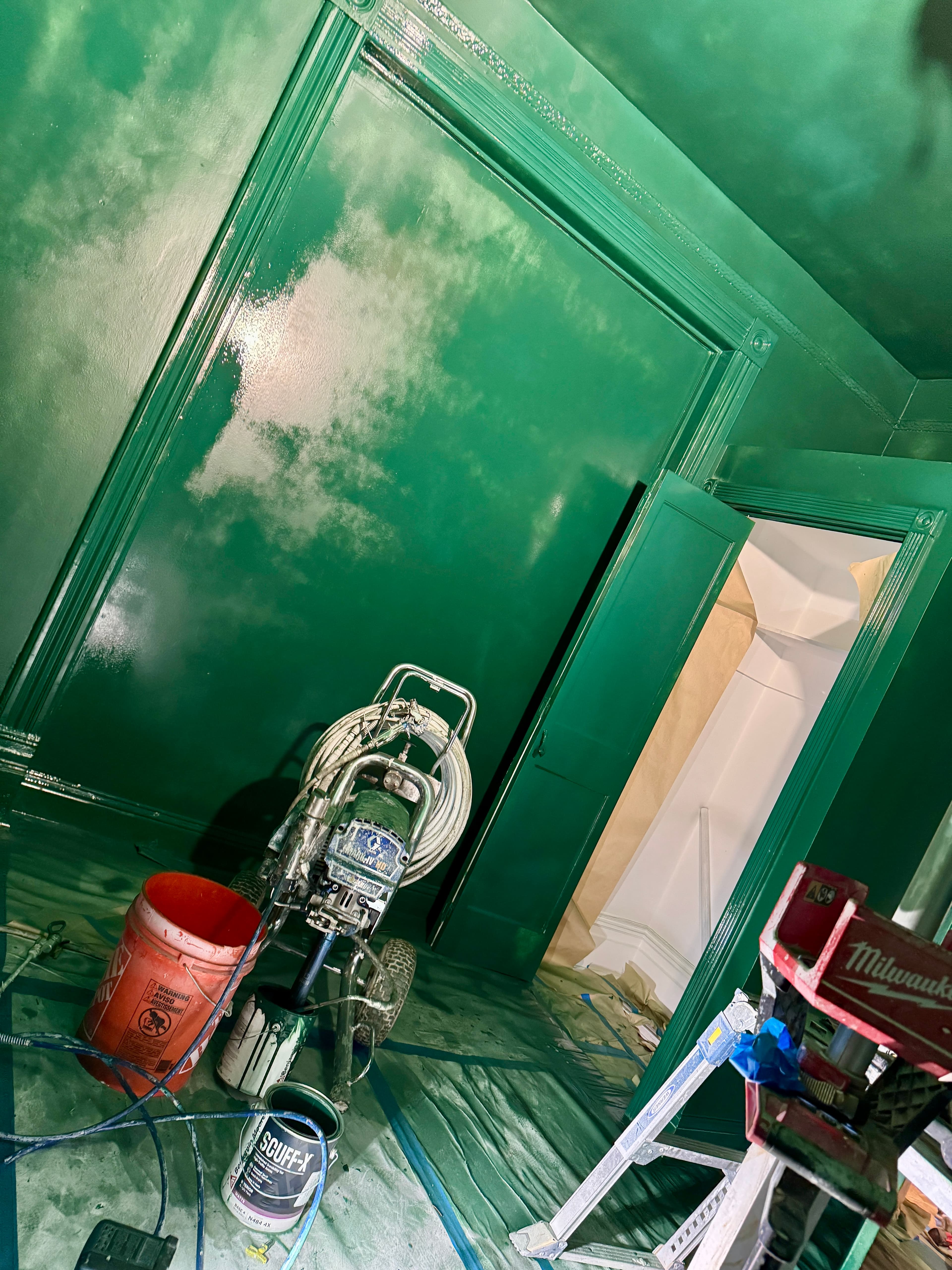 Professional paint sprayer in a room with walls and ceiling freshly painted a deep green.