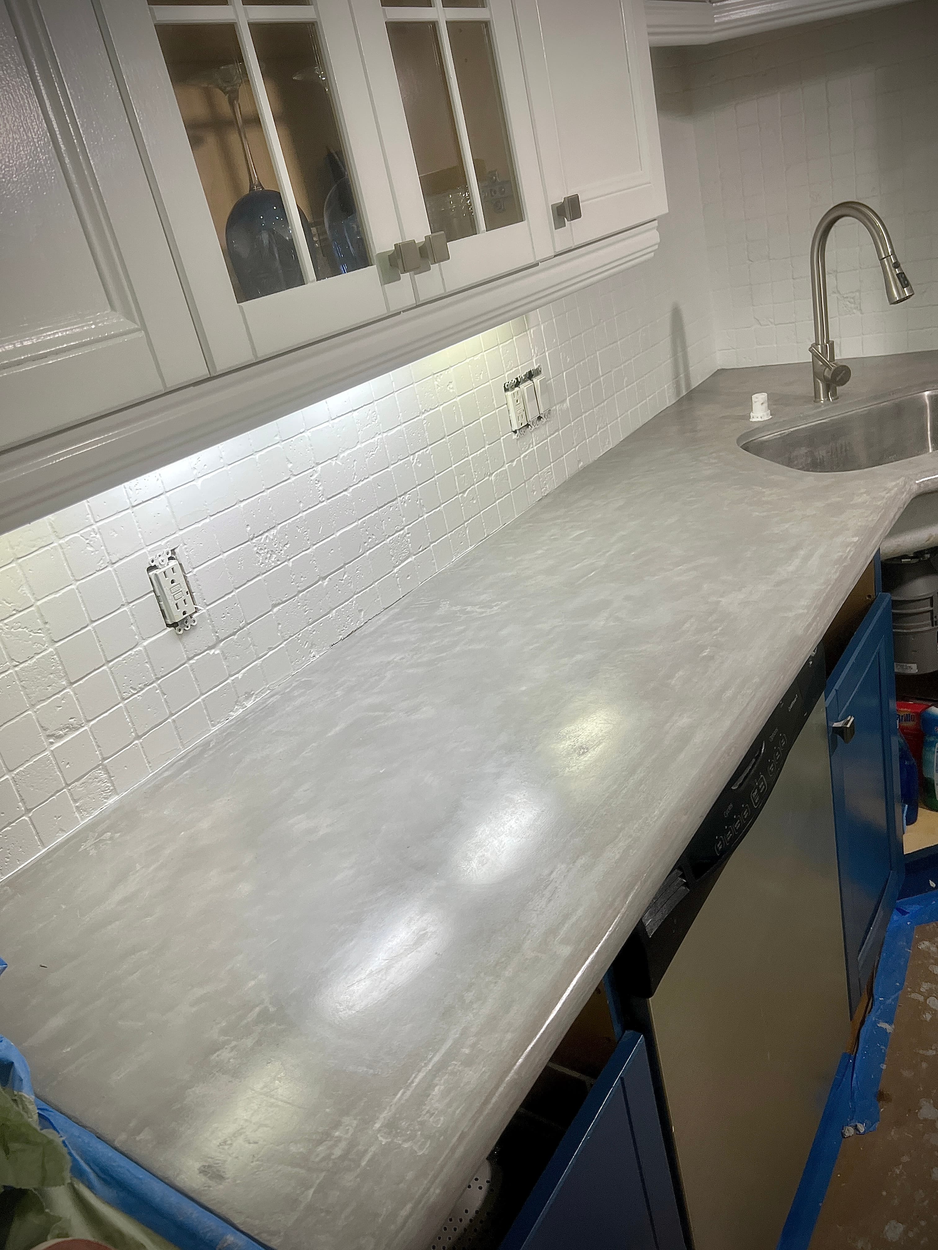 Modern grey concrete kitchen countertop with white tiled backsplash and white upper glass cabinets.