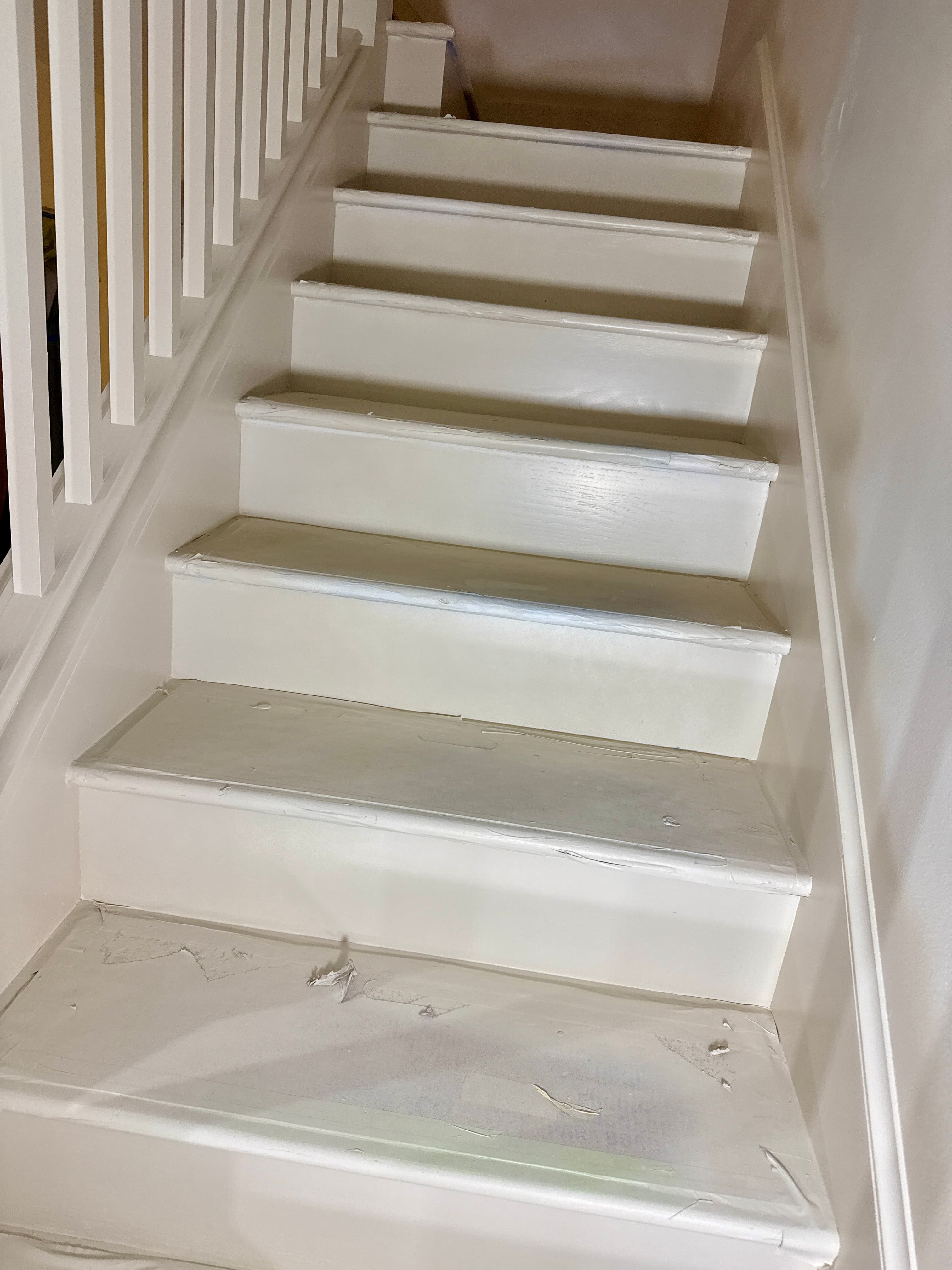 Freshly painted white indoor staircase with protective tape on the edges of the wooden steps.
