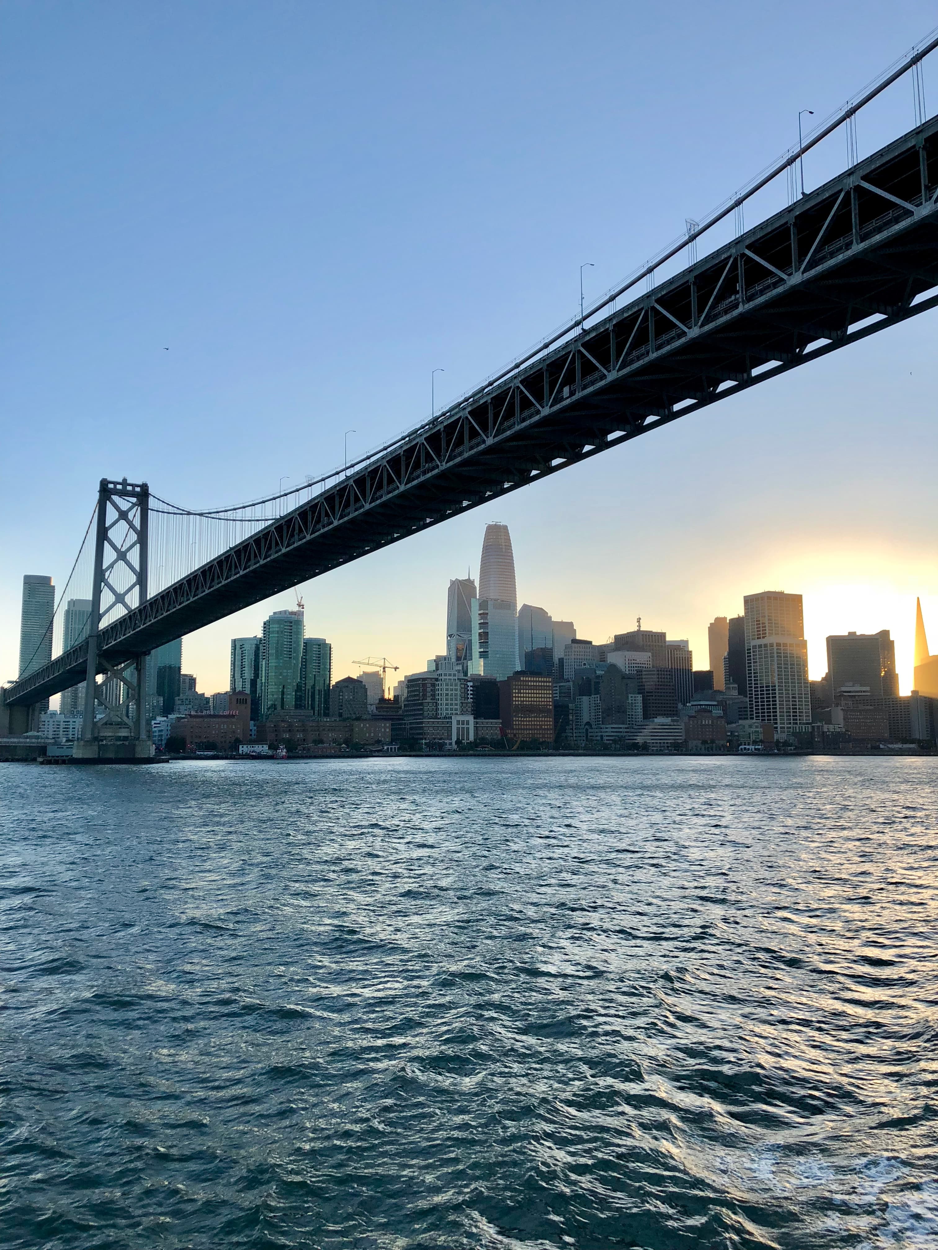 San Francisco Bay Bridge stretching over choppy water toward the city skyline at sunset.