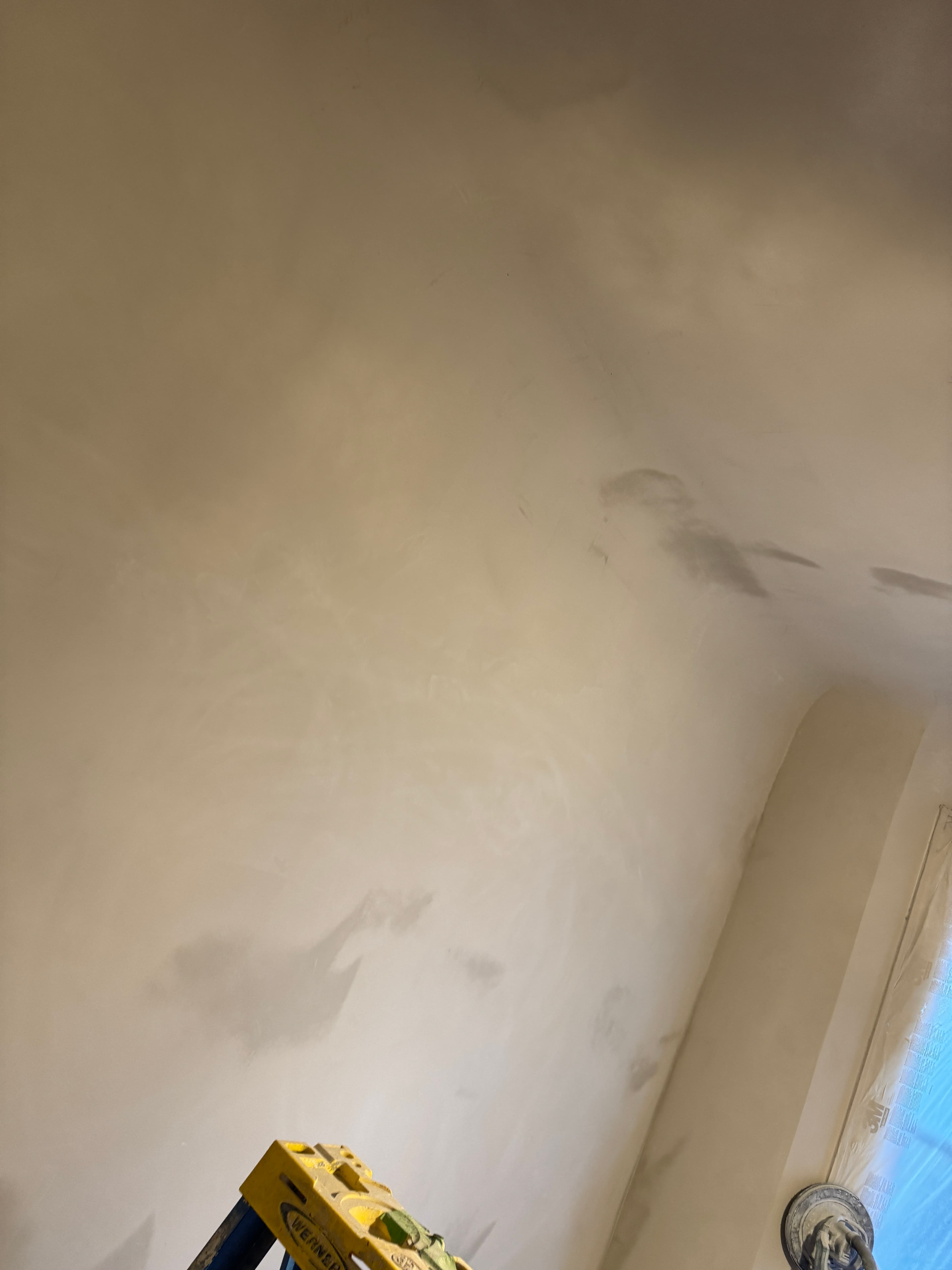 Smoothly finished drywall in a room under construction with a yellow ladder in the corner.