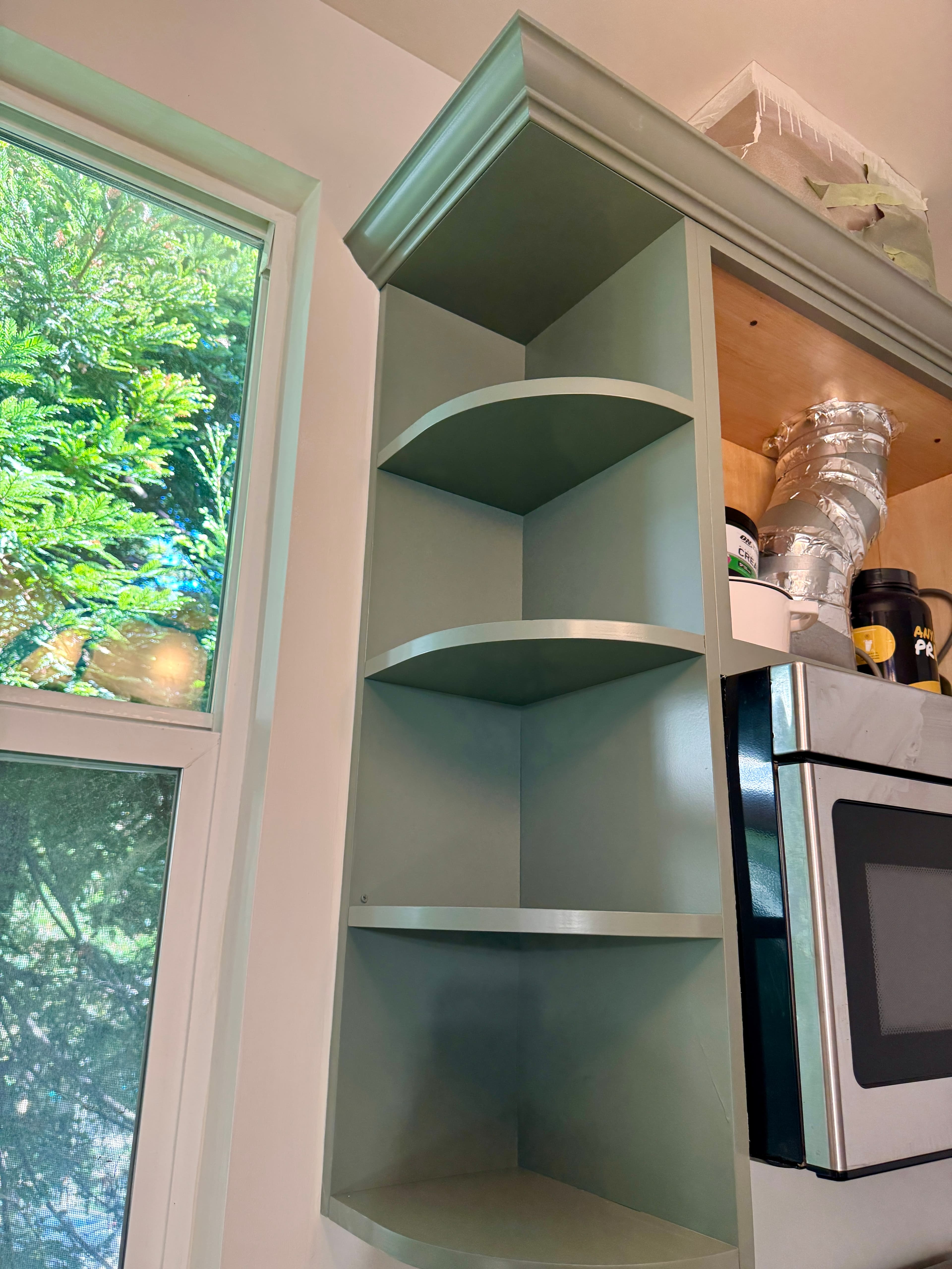 Built-in sage green corner shelves with curved edges located beside a kitchen window.