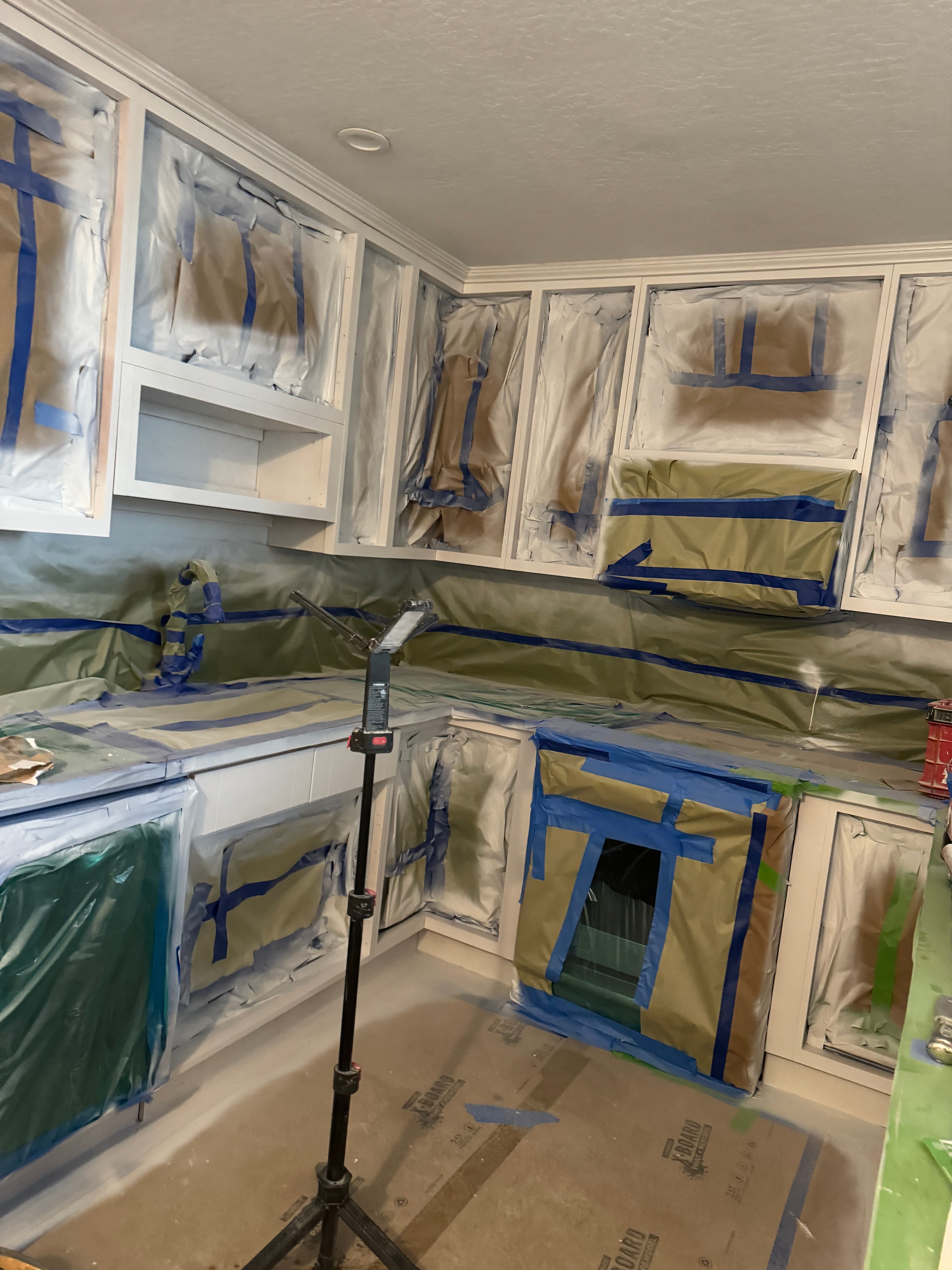 Built-in cabinets masked with paper and blue painter's tape during a home renovation project.