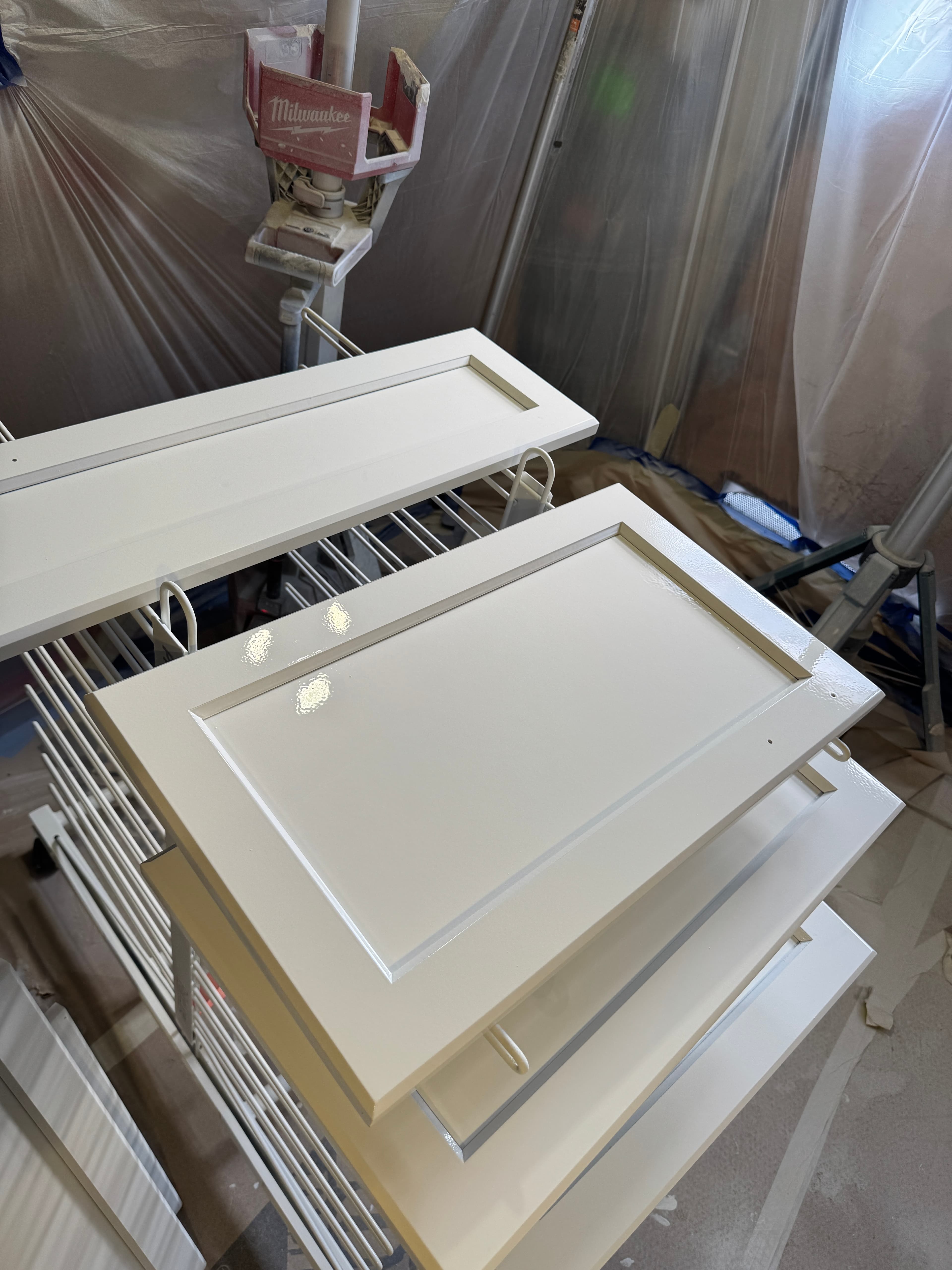Freshly painted white shaker-style cabinet doors drying on a metal rack in a workshop.