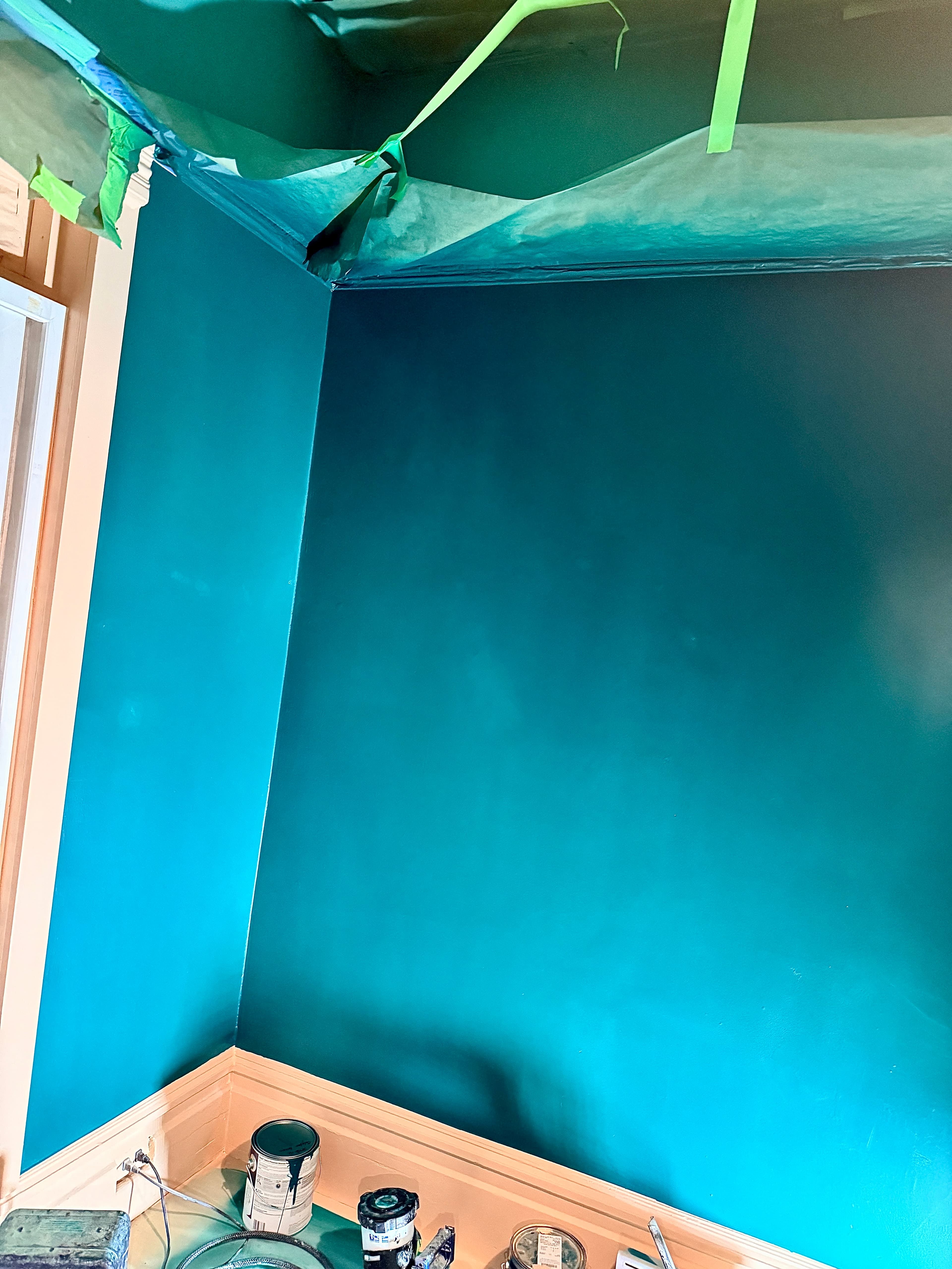 Deep teal walls in a room corner with protective plastic sheeting and paint cans below.