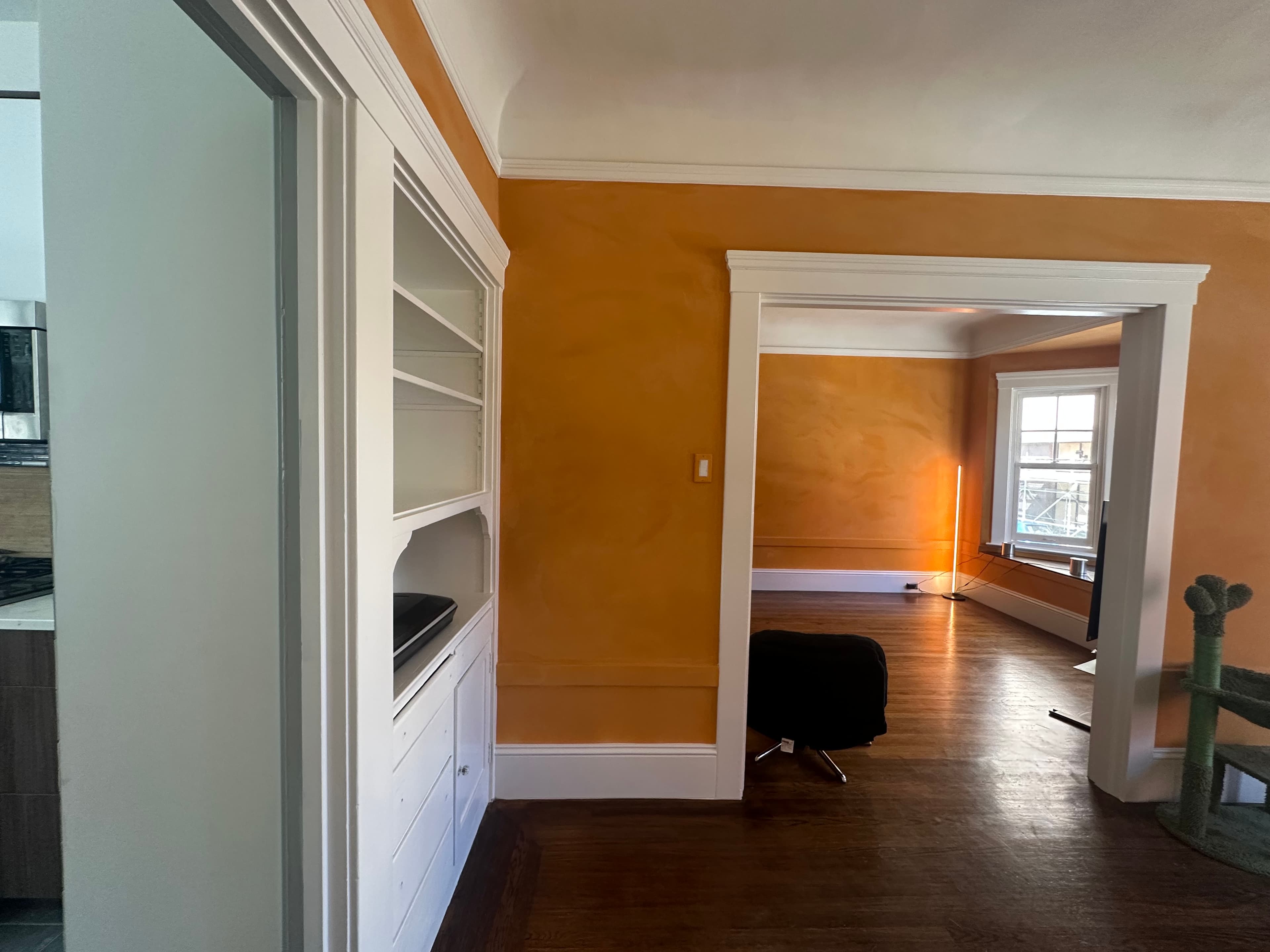 Textured orange walls, white built-in shelving, dark wood floors, and a cactus-shaped cat tree.