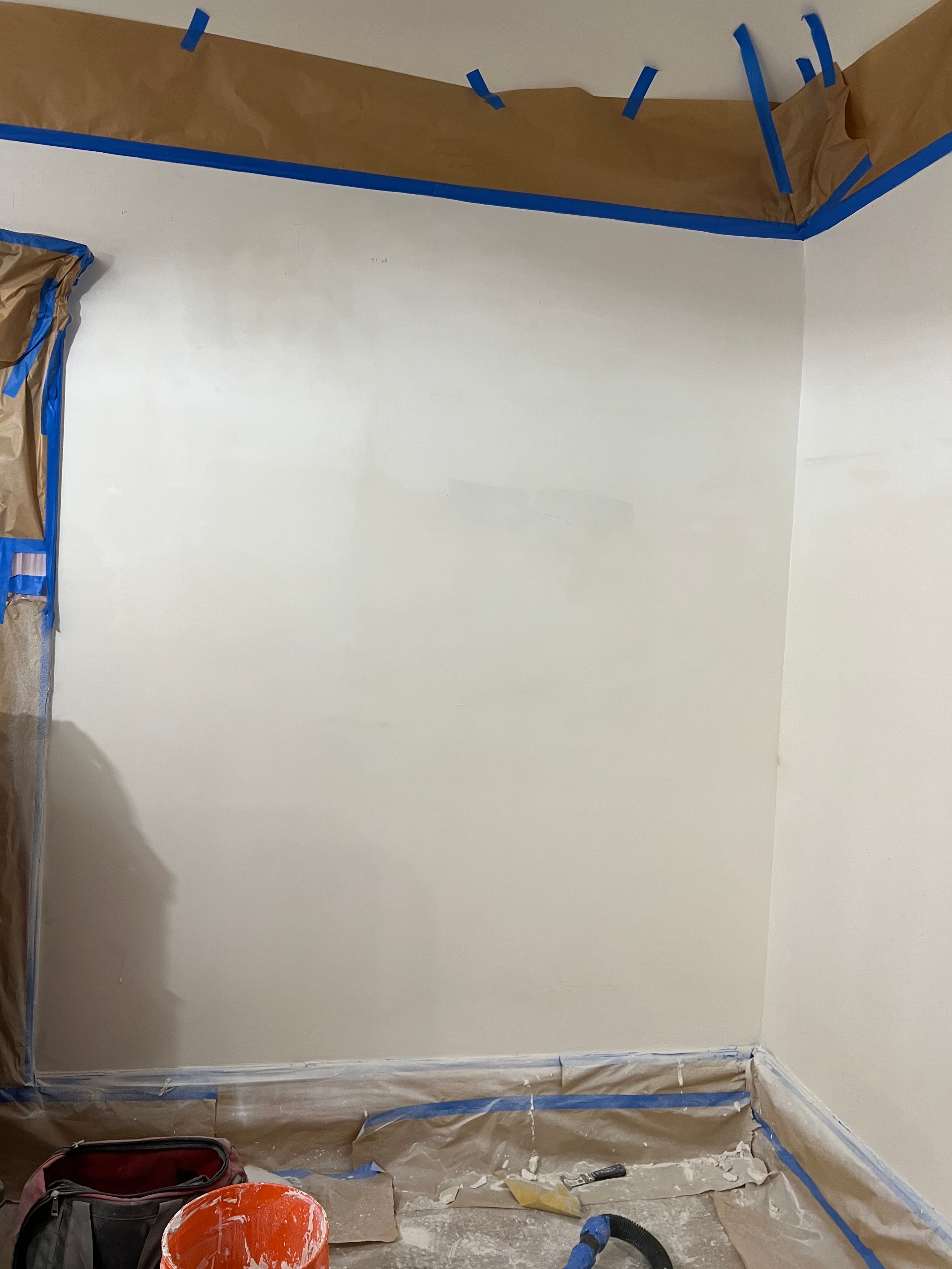 White wall prepped for painting with blue painter's tape and brown paper along the borders.