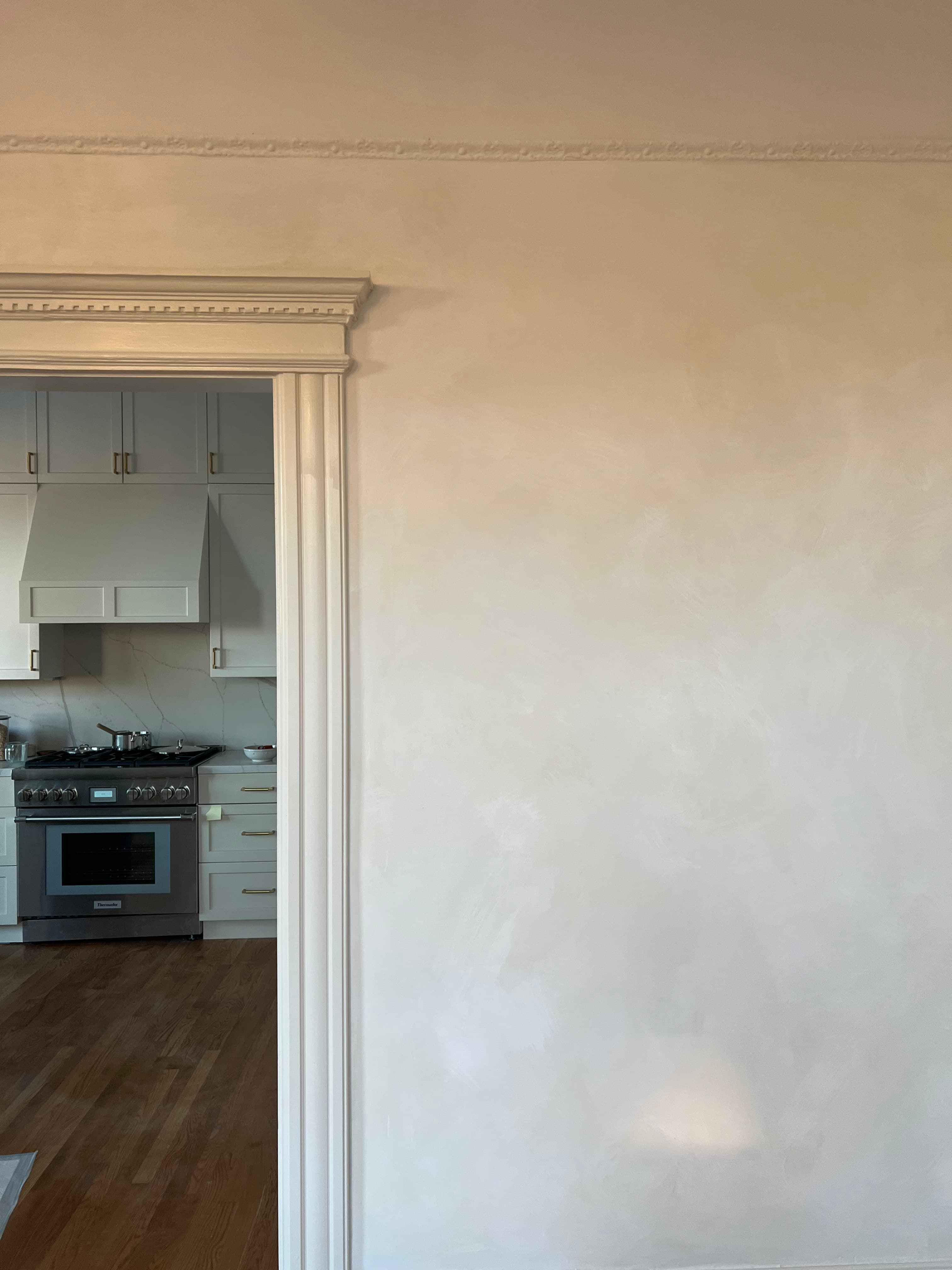 View through a white doorway into a kitchen with white cabinets and stainless steel appliances.