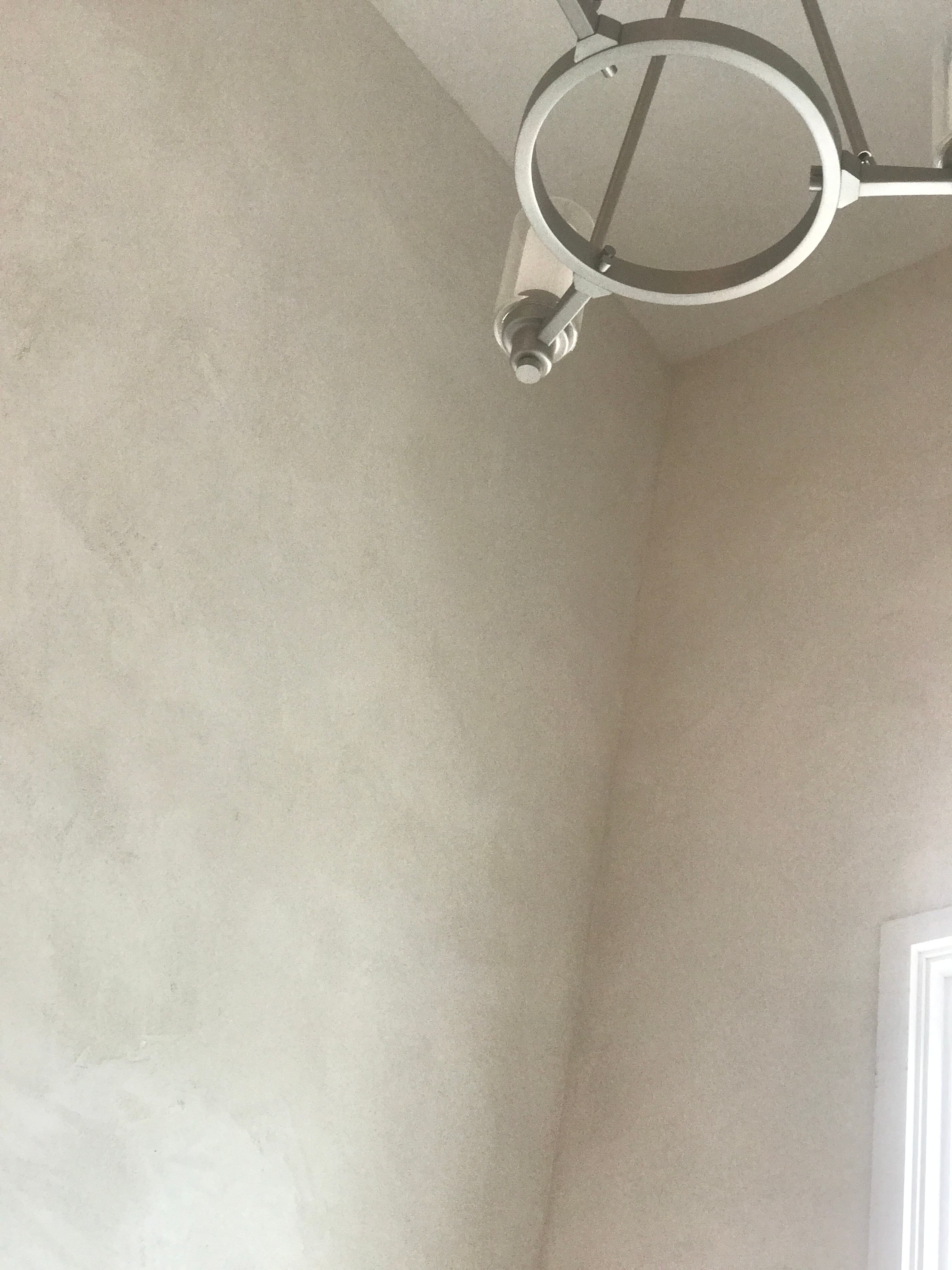 Modern circular silver light fixture on a white textured ceiling near a bright window.